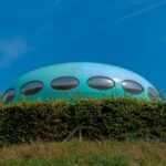Casa redonda futurista azul semelhante a um OVNI em colina gramada