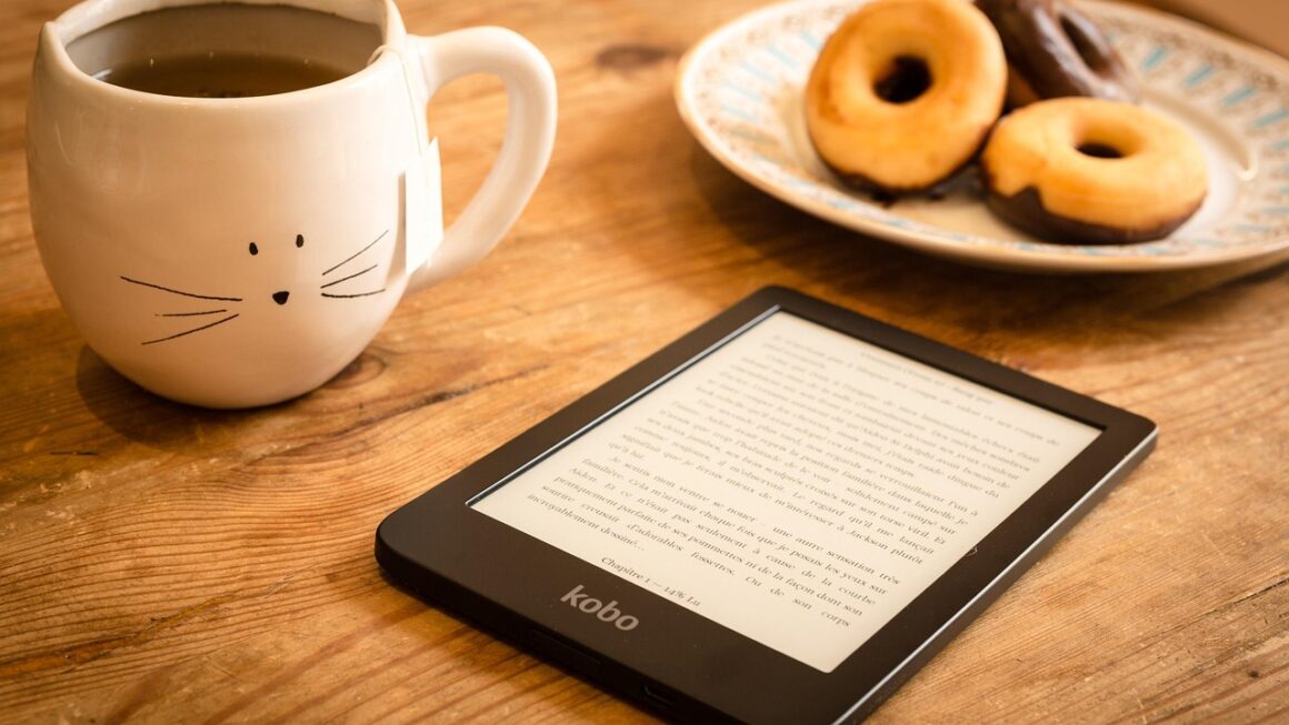 E-reader em mesa de madeira com caneca de chá e donuts ao fundo