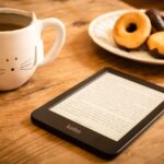 E-reader em mesa de madeira com caneca de chá e donuts ao fundo