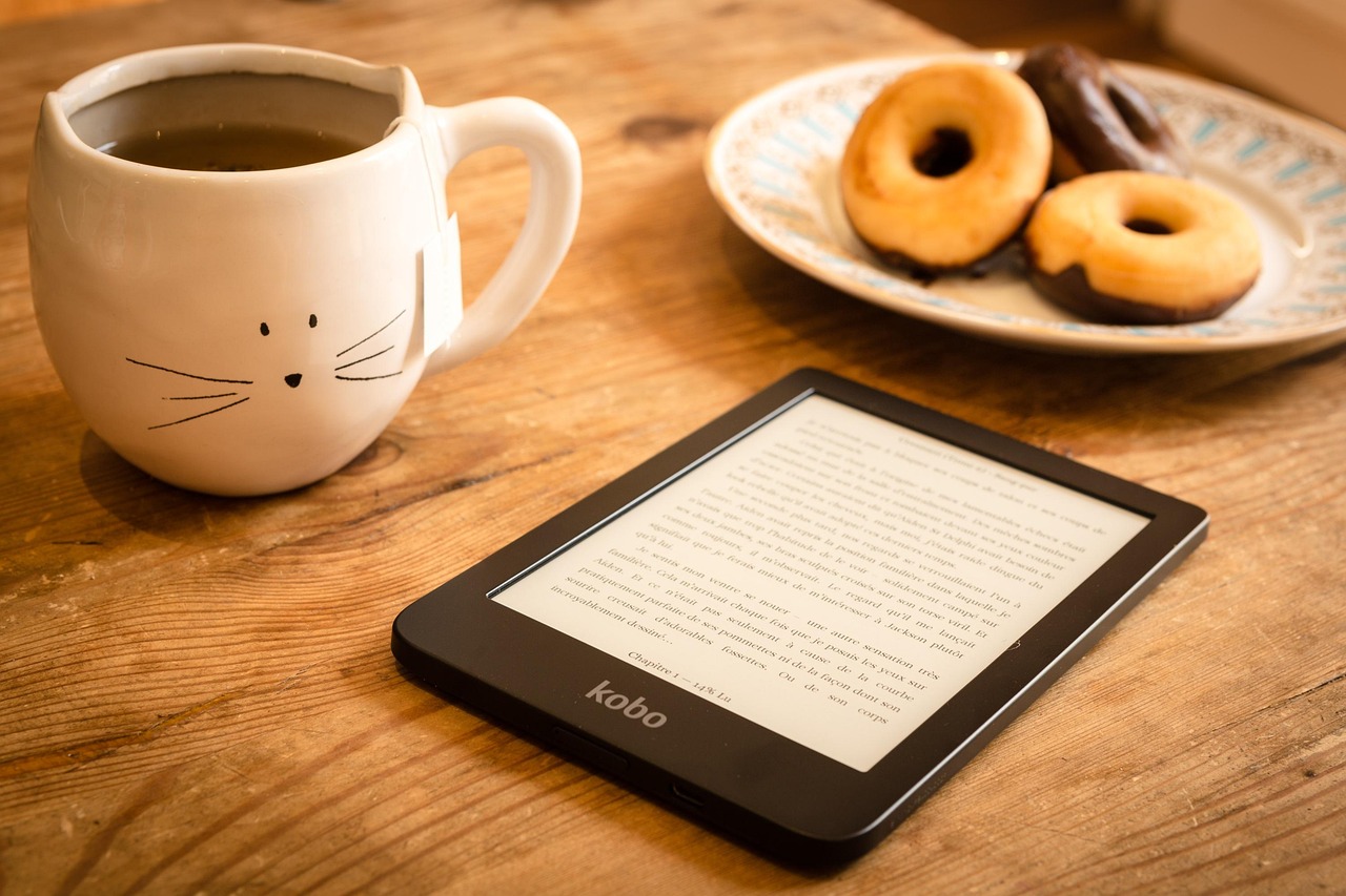 E-reader em mesa de madeira com caneca de chá e donuts ao fundo